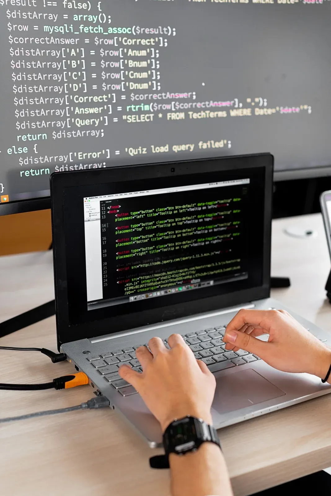 Persona revisando código en un portátil y un monitor de trabajo.