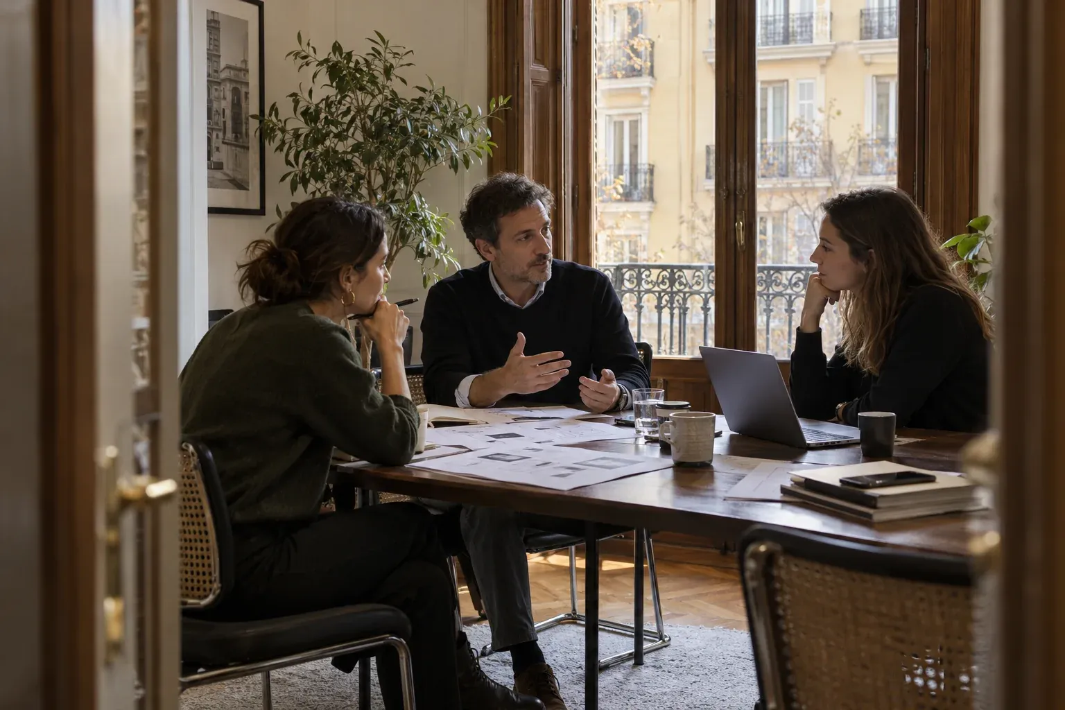 Tres profesionales revisan una propuesta web en una oficina con grandes ventanas y balcones