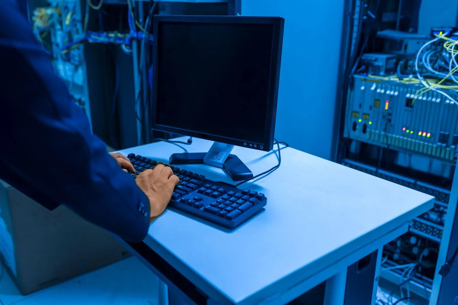 Técnico utiliza un ordenador junto a varios armarios de servidores.
