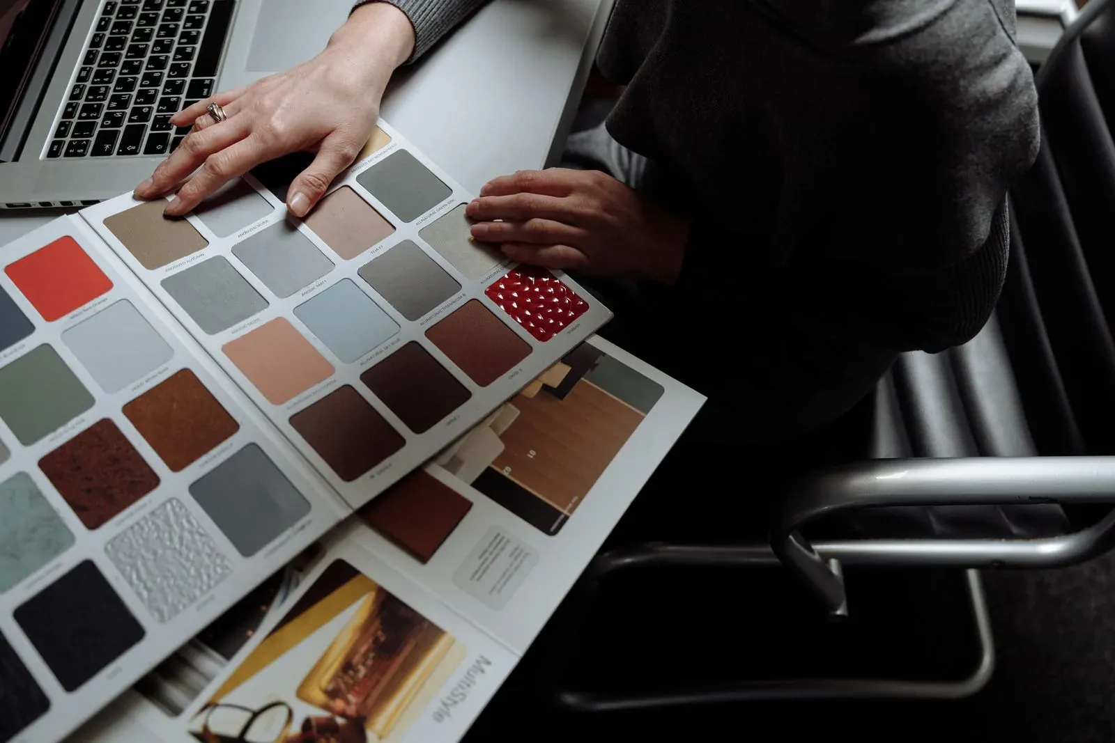 Persona compara muestras de color junto a un portátil y planos impresos.
